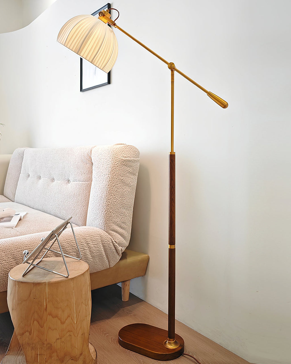 Clérachic floor lamp reaching over a pale sofa and a log stool in a white room, with a framed print behind the shade.