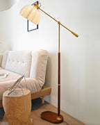 Clérachic floor lamp reaching over a pale sofa and a log stool in a white room, with a framed print behind the shade.