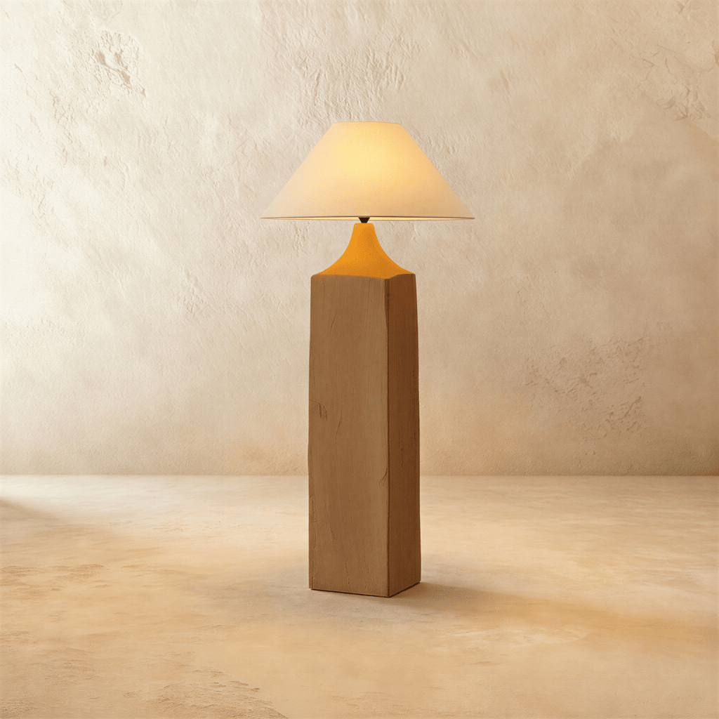Clérachic floor lamp with a square raw-wood post, a tapered amber-orange neck and a wide linen cone shade glowing warm on limewash.