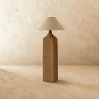 Clérachic floor lamp with a square raw-grain wooden post, a tapered wood neck and a wide natural linen cone shade, unlit, on limewash.
