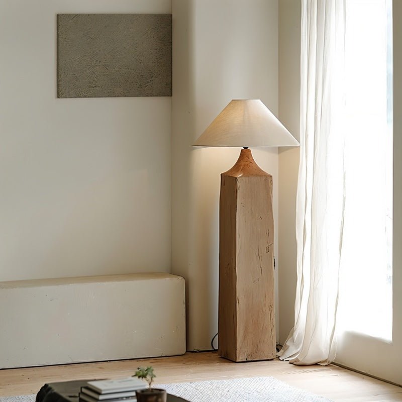 Clérachic floor lamp with a square wooden post and linen cone shade, in a pale corner beside a sheer curtain and a low plaster bench.