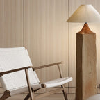 Clérachic floor lamp with a square wooden post and linen cone shade, glowing beside a woven-seat wooden armchair against pale wood panels.
