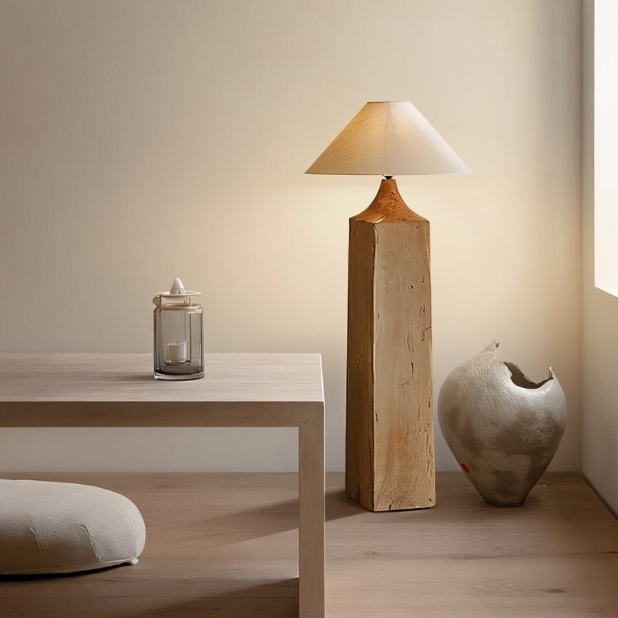 Clérachic floor lamp with a square wooden post and linen cone shade, between a pale wood table and a sculptural ceramic vase.