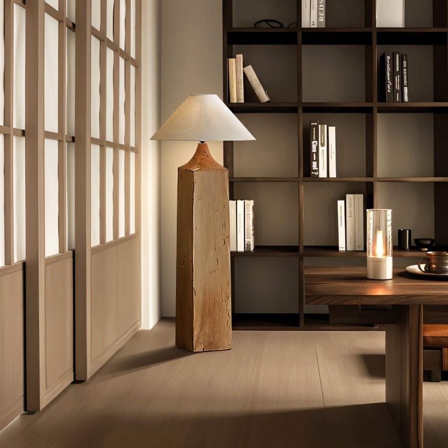 Clérachic floor lamp with a square wooden post and linen cone shade, in a study with dark open shelving, books and a glass candle lantern.
