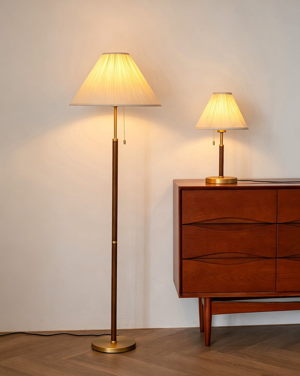 This Clérachic floor lamp glows warm cream next to a matching smaller table lamp on a walnut chest of drawers, with a herringbone floor below.