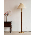 Unlit Clérachic floor lamp with a pleated beige shade, next to a dark side table and a white vase of orange-red berry branches.