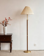 Pleated beige shade and walnut stem of this Clérachic floor lamp, seen beside a carved side table and a vase of dried red-orange branches.