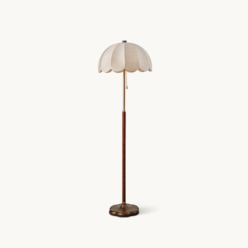 Floor lamp from Clérachic with a scalloped white fabric shade, a slim brass neck, a walnut-toned wood stem and a rounded wooden base, on a plain white backdrop.