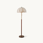 Floor lamp from Clérachic with a scalloped white fabric shade, a slim brass neck, a walnut-toned wood stem and a rounded wooden base, on a plain white backdrop.