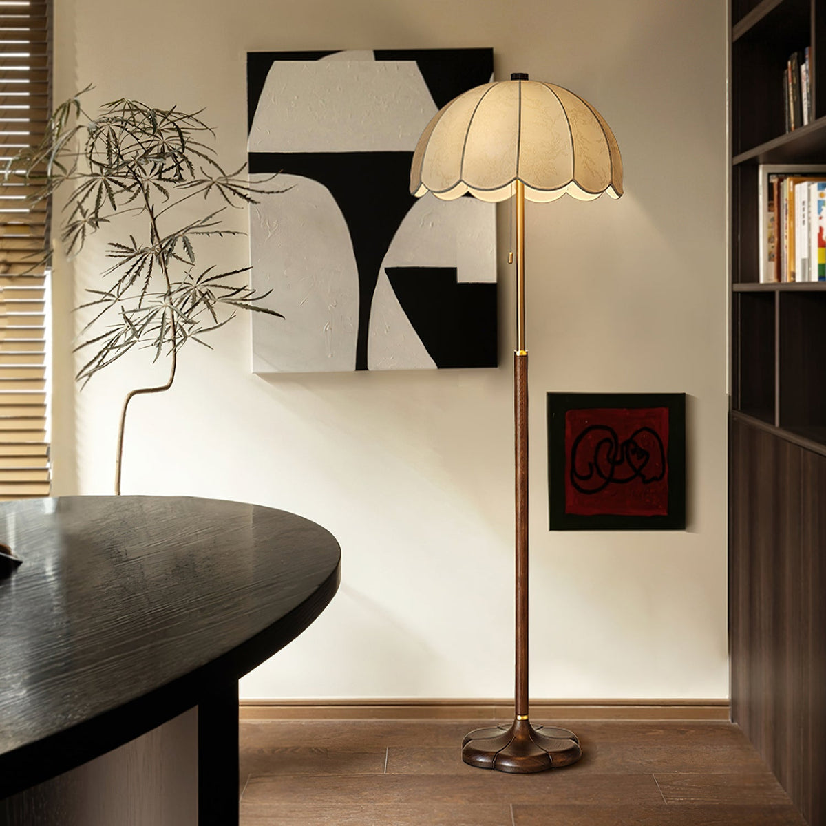 Clérachic floor lamp with a pleated petal shade standing against a cream wall, near a black oval table, a bookcase and abstract wall art.