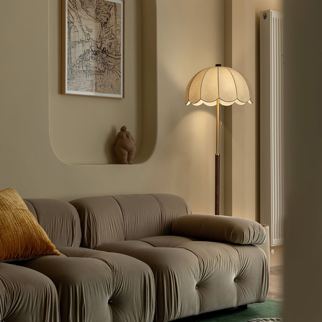 A Clérachic floor lamp stands behind a grey modular sofa in a curved-wall living room, with a framed map print above.