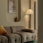 A Clérachic floor lamp stands behind a grey modular sofa in a curved-wall living room, with a framed map print above.