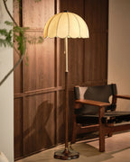 A Clérachic floor lamp lit against walnut panelling, with a black leather and wood armchair at its side.