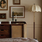 Unlit Clérachic floor lamp with a cream scalloped shade, set by a walnut sideboard with a rattan door and framed landscape pictures.