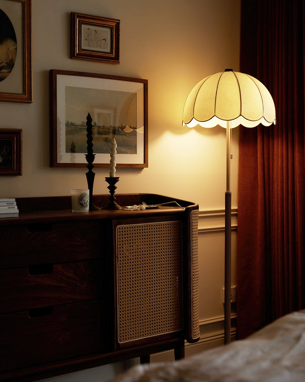 The same walnut sideboard scene with this Clérachic floor lamp switched on, its shade glowing warm beside a dark red curtain.