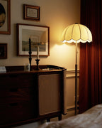 The same walnut sideboard scene with this Clérachic floor lamp switched on, its shade glowing warm beside a dark red curtain.