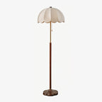 Full-length Clérachic floor lamp on a pale grey backdrop, showing its scalloped fabric shade, brass neck, walnut stem and round base.