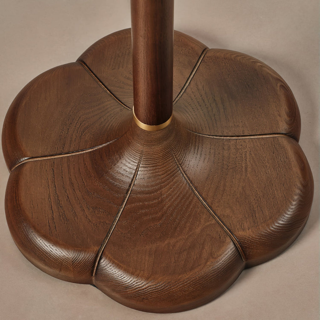Close view of the five-lobed walnut-toned wood base on this Clérachic floor lamp, with a brass ring where the stem meets it.