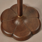 Close view of the five-lobed walnut-toned wood base on this Clérachic floor lamp, with a brass ring where the stem meets it.