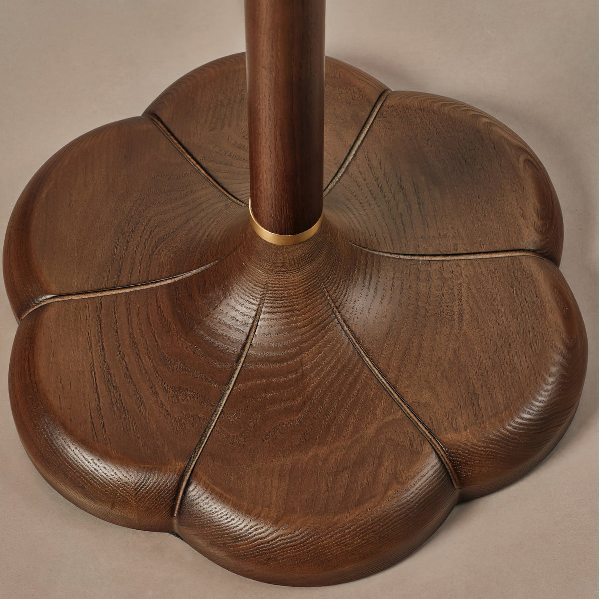 Close view of the five-lobed walnut-toned wood base on this Clérachic floor lamp, with a brass ring where the stem meets it.