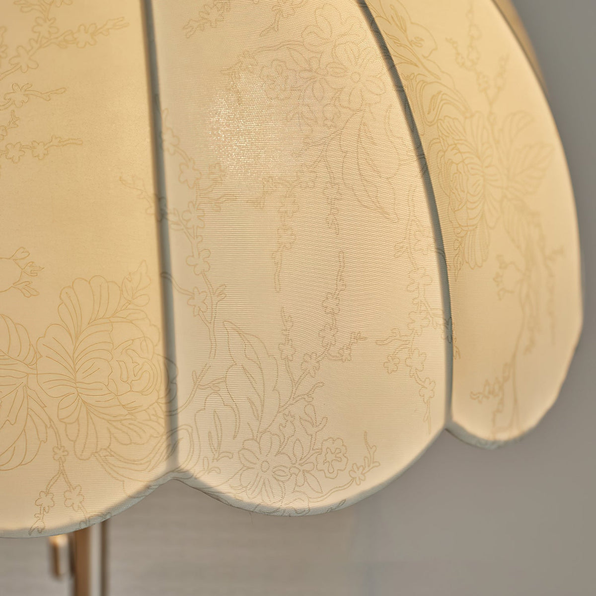 Close view of the lit fabric shade on this Clérachic floor lamp, with a faint floral pattern woven through the cream panels.