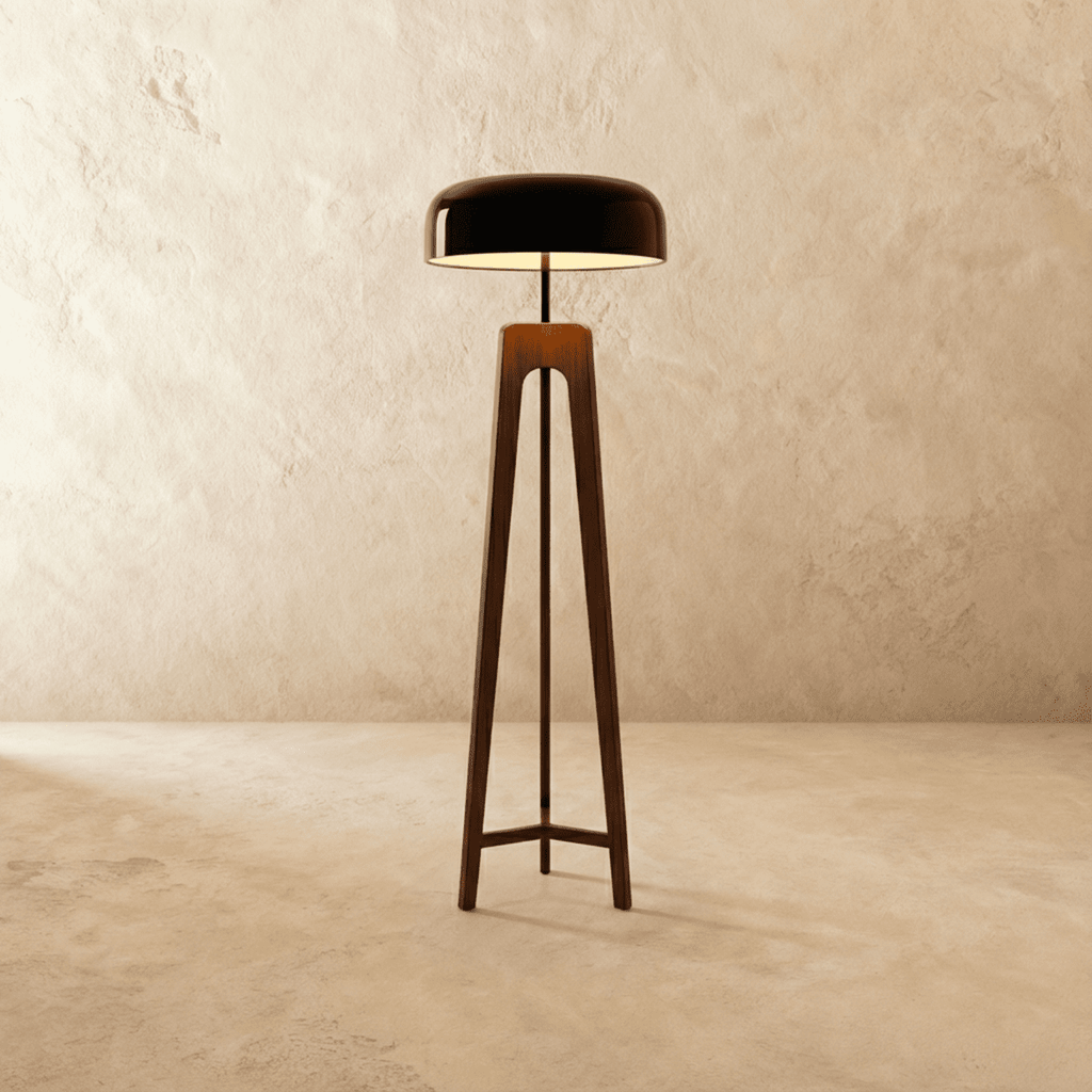 Clérachic tall tripod floor lamp in dark stained wood with a black disc shade, lit, on a limewash backdrop.