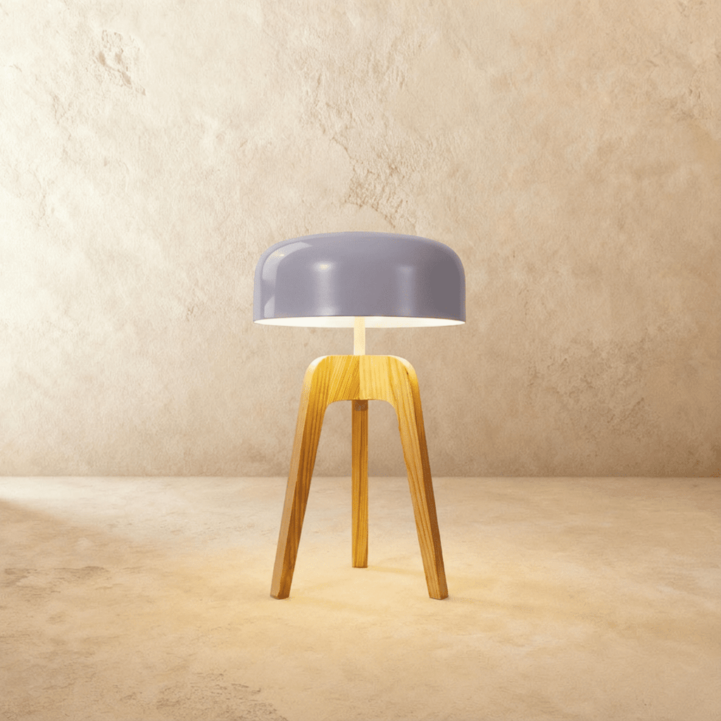 Clérachic compact light wood tripod lamp with a soft lilac-grey disc shade glowing warmly on a limewash backdrop.