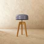 Clérachic compact light wood tripod lamp with a lilac-grey disc shade, switched off, against a limewash wall.