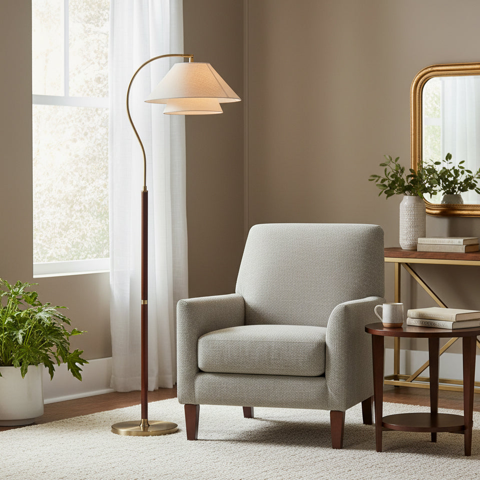 Beside a pale grey armchair and a round walnut side table, this Clérachic floor lamp shows its brass base and arched arm.