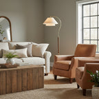 This Clérachic floor lamp arches over a rust leather armchair, with a cream sofa and a reclaimed-wood coffee table nearby.