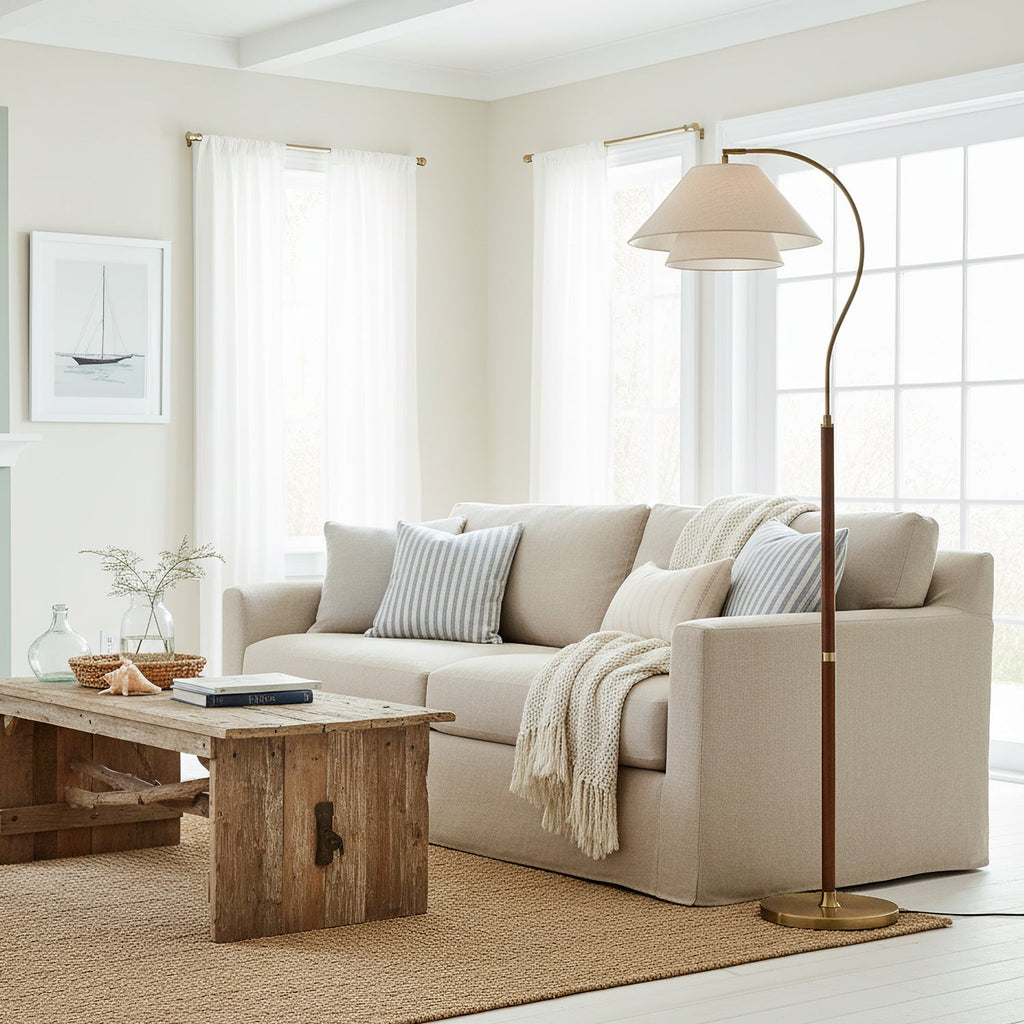 A Clérachic floor lamp beside a pale linen sofa in a white room, its brass base resting on a woven jute rug.