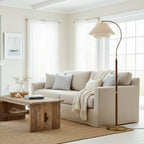 A Clérachic floor lamp beside a pale linen sofa in a white room, its brass base resting on a woven jute rug.