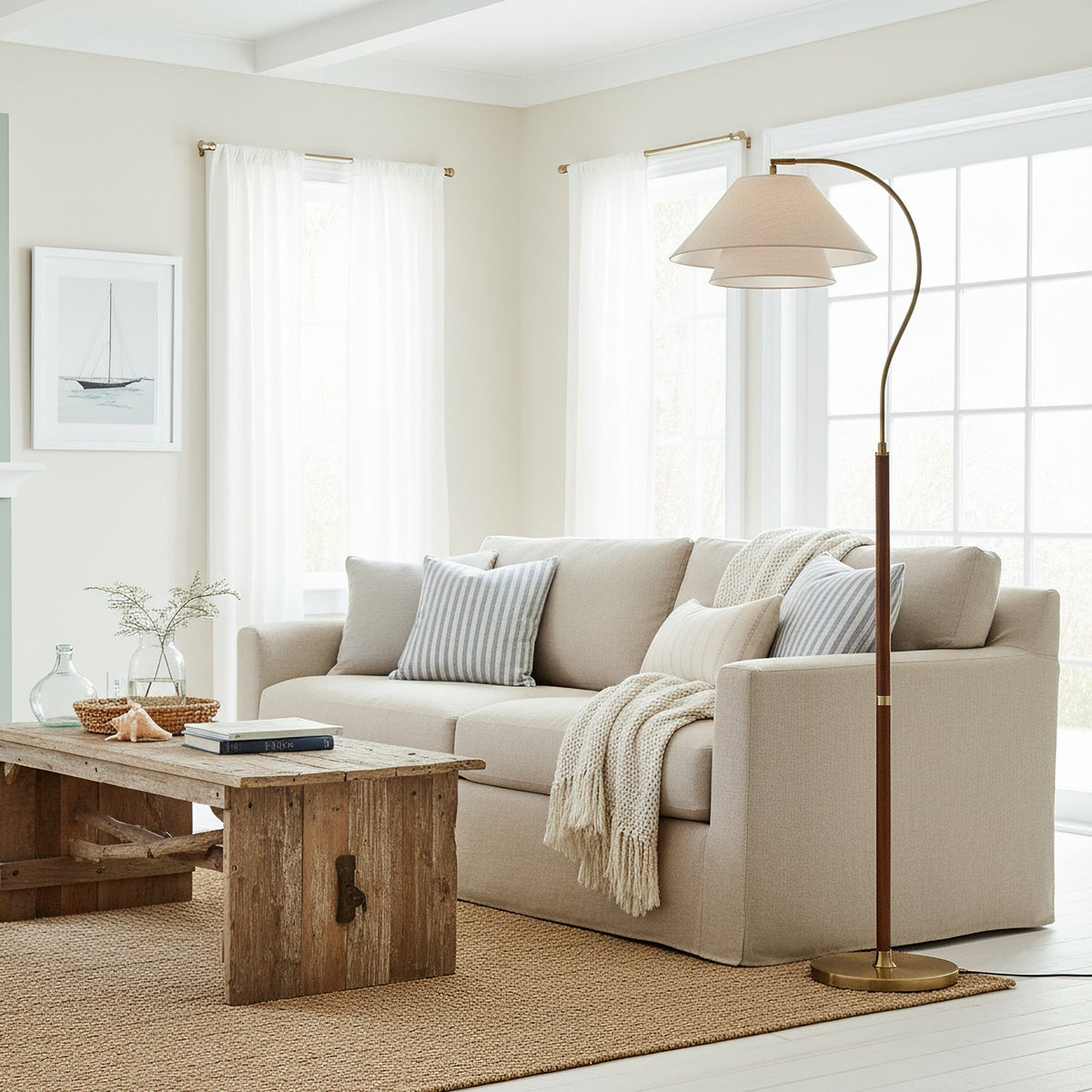 A Clérachic floor lamp beside a pale linen sofa in a white room, its brass base resting on a woven jute rug.