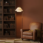 The Clérachic floor lamp stands against a terracotta wall by a tall bookcase, next to a brown leather armchair.