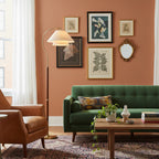This Clérachic floor lamp sits in front of a framed-print gallery wall in terracotta, with a green velvet sofa below.