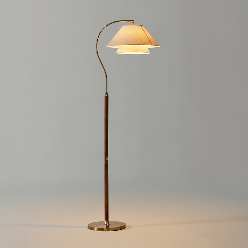 Walnut-stemmed Clérachic floor lamp with a brass base, lit against a plain grey backdrop.