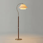 Walnut-stemmed Clérachic floor lamp with a brass base, lit against a plain grey backdrop.