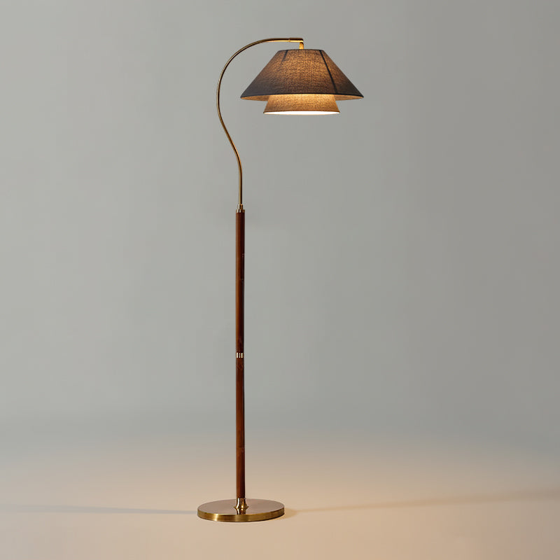 This Clérachic floor lamp has a walnut stem and a dark charcoal shade over a brass base, lit on a grey backdrop.