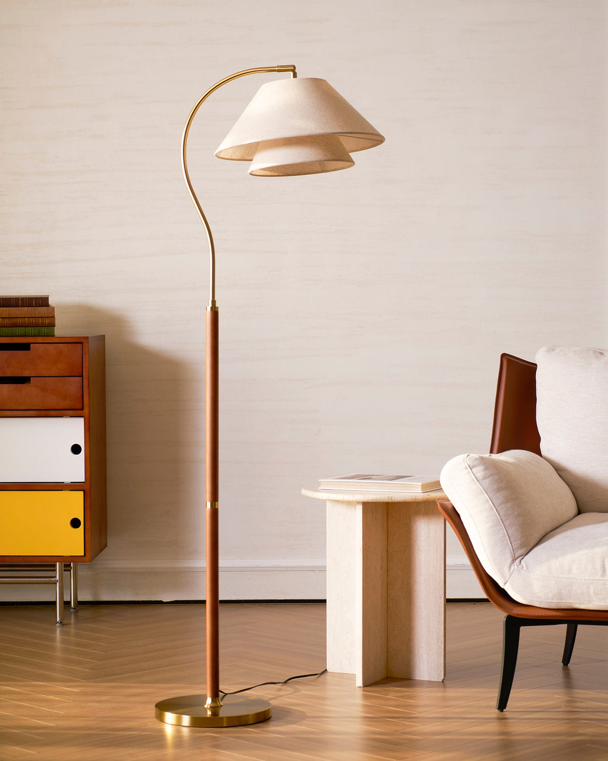 The Clérachic floor lamp in a warm room with a yellow-and-white drawer unit, a travertine side table and a leather chair.
