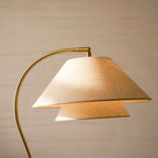 Close view of the layered linen shade and curved brass arm on this Clérachic floor lamp, lit from inside.