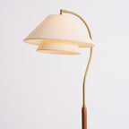 Upper part of this Clérachic floor lamp on a pale backdrop, with a two-tier linen shade and an S-curved brass arm.