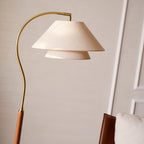 Curved brass arm and tiered linen shade of this Clérachic floor lamp, seen from below against a cream wall.
