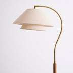 Close view of the arched brass arm and the stacked linen shade on this Clérachic floor lamp, on a light backdrop.