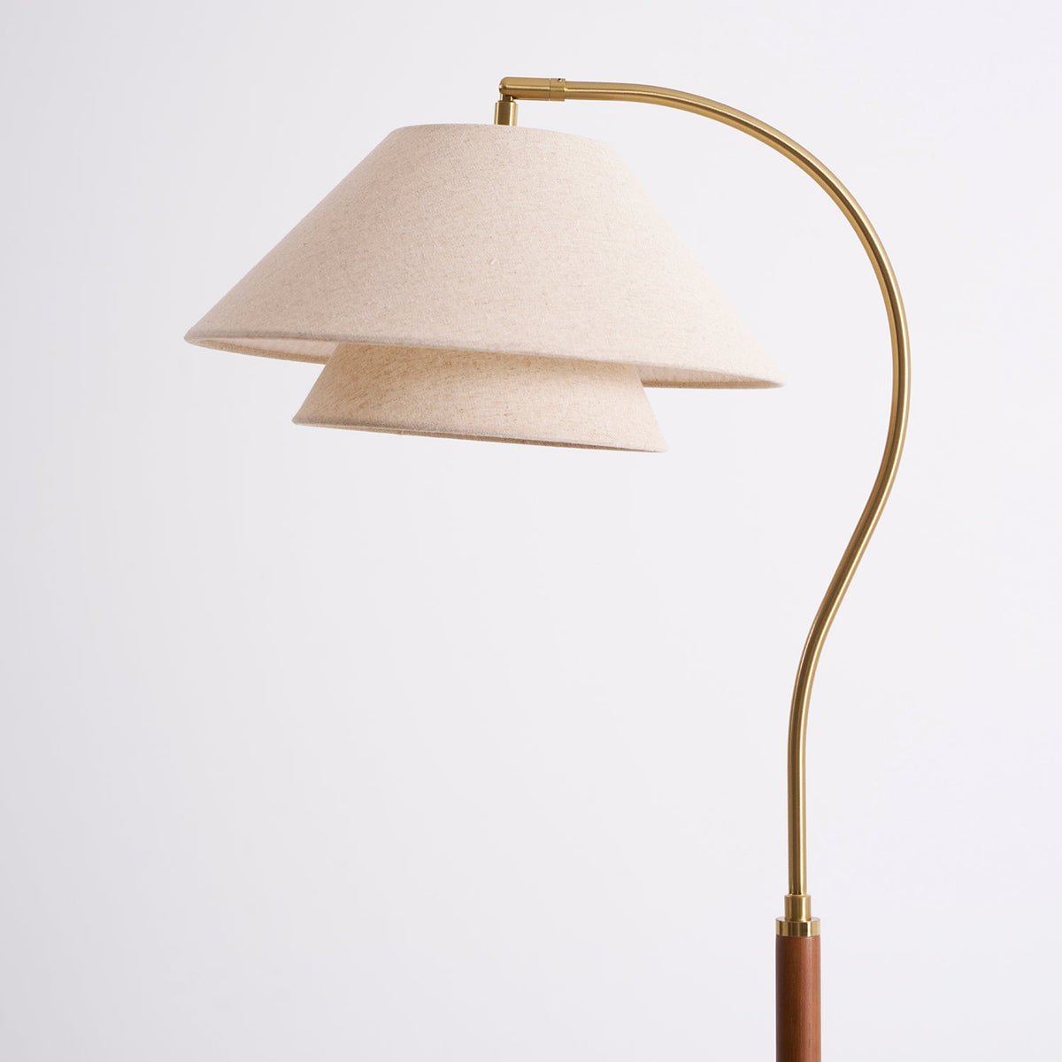 Close view of the arched brass arm and the stacked linen shade on this Clérachic floor lamp, on a light backdrop.