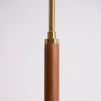 Close view of the walnut stem of this Clérachic floor lamp, with a brass collar and a slim brass rod above it.