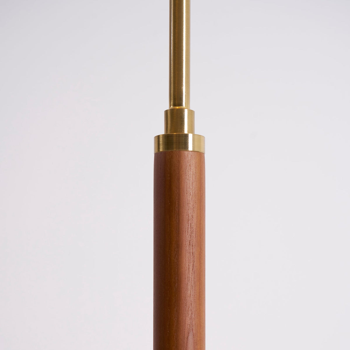 Close view of the walnut stem of this Clérachic floor lamp, with a brass collar and a slim brass rod above it.
