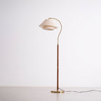 Full-length Clérachic floor lamp, unlit, on a pale backdrop, with a walnut stem, a brass base and a black cord.