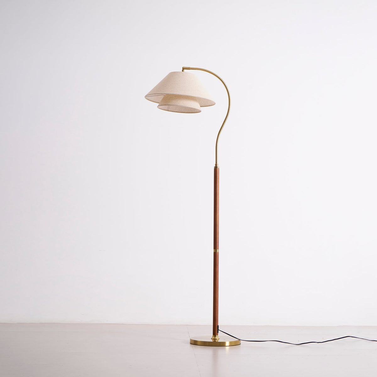 Full-length Clérachic floor lamp, unlit, on a pale backdrop, with a walnut stem, a brass base and a black cord.