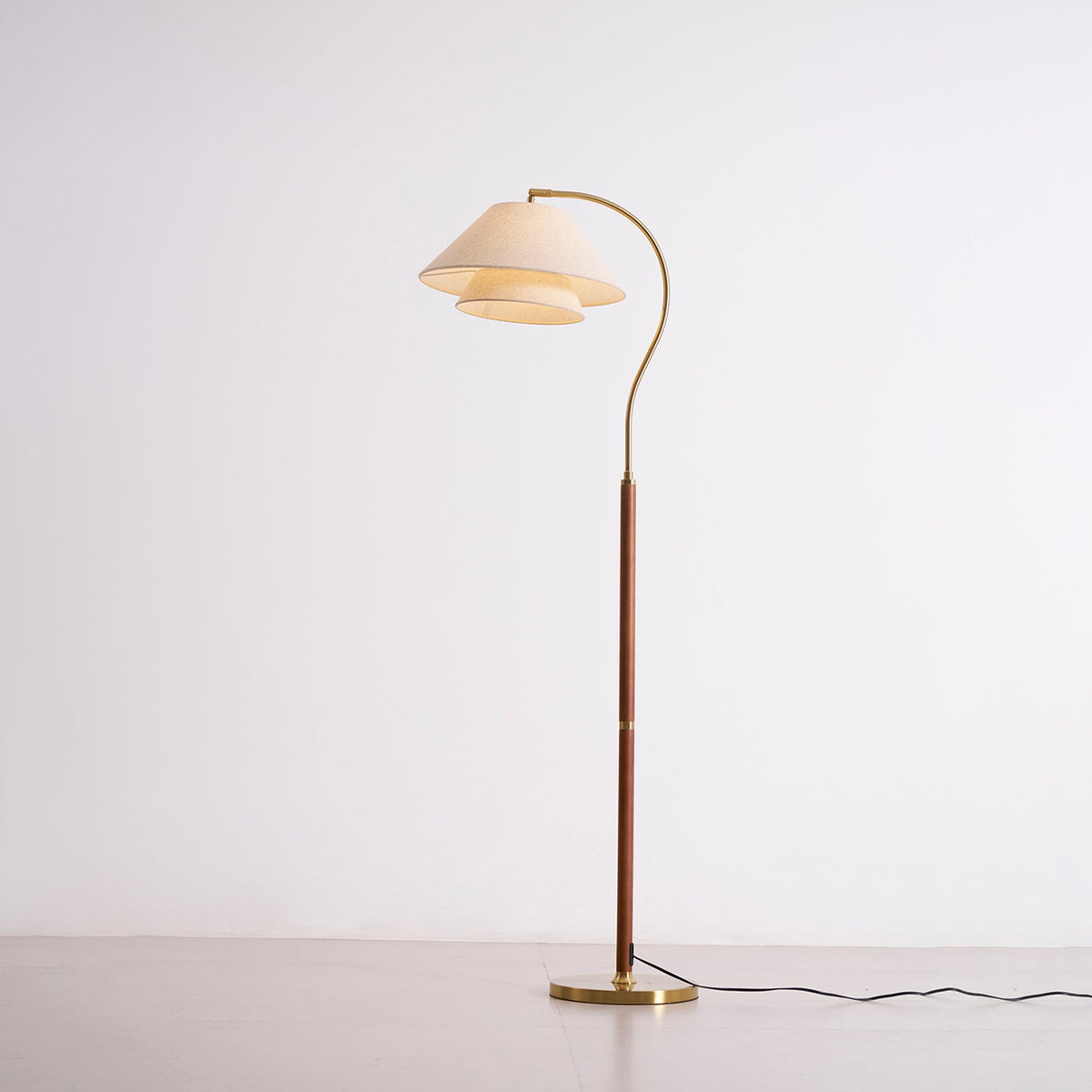 Full-length Clérachic floor lamp, lit, with the two-tier linen shade glowing against a pale studio wall.