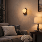 Clérachic wall lamp glowing above a sofa with plaid and check cushions in a warm living room.